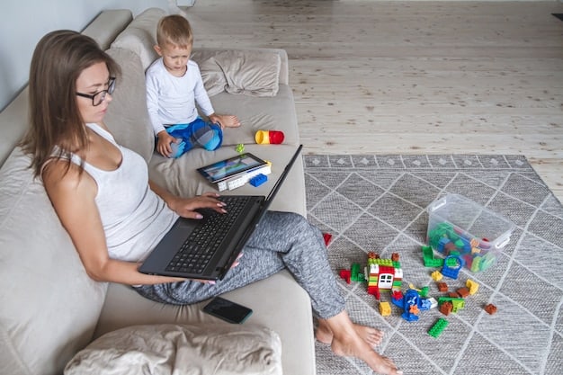 A single mother working on her laptop at home while her young child plays with toys nearby.