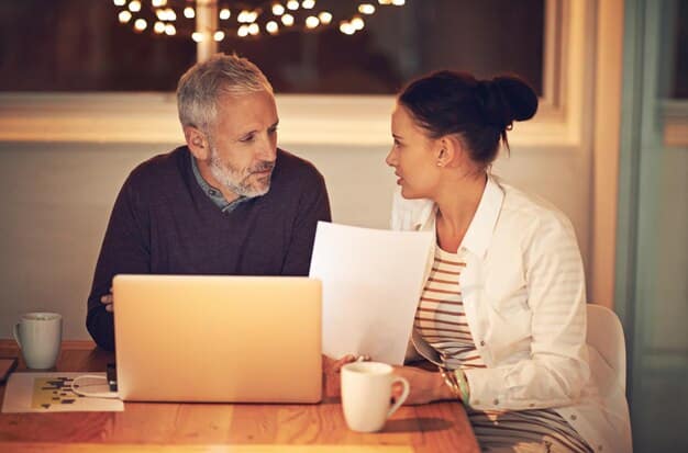 A financial advisor meeting with a couple in their home, discussing a retirement plan on a laptop. The scene is warmly lit and comfortable.