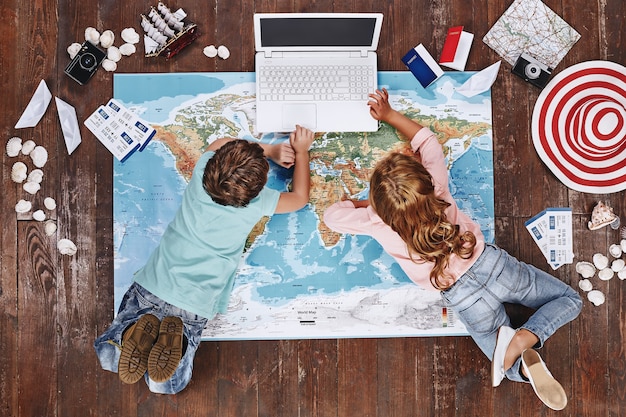 A family is shown planning a vacation using a laptop, with travel brochures and maps spread out on a table. They are discussing affordable travel options and destinations.