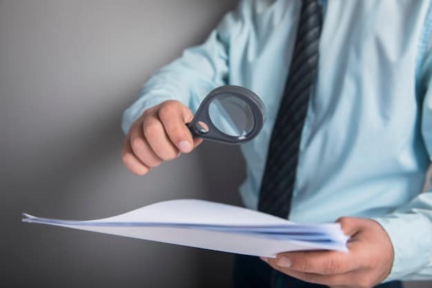 A close-up of a hand holding a magnifying glass over a document with financial graphs and charts. The focus is on the details being examined closely.